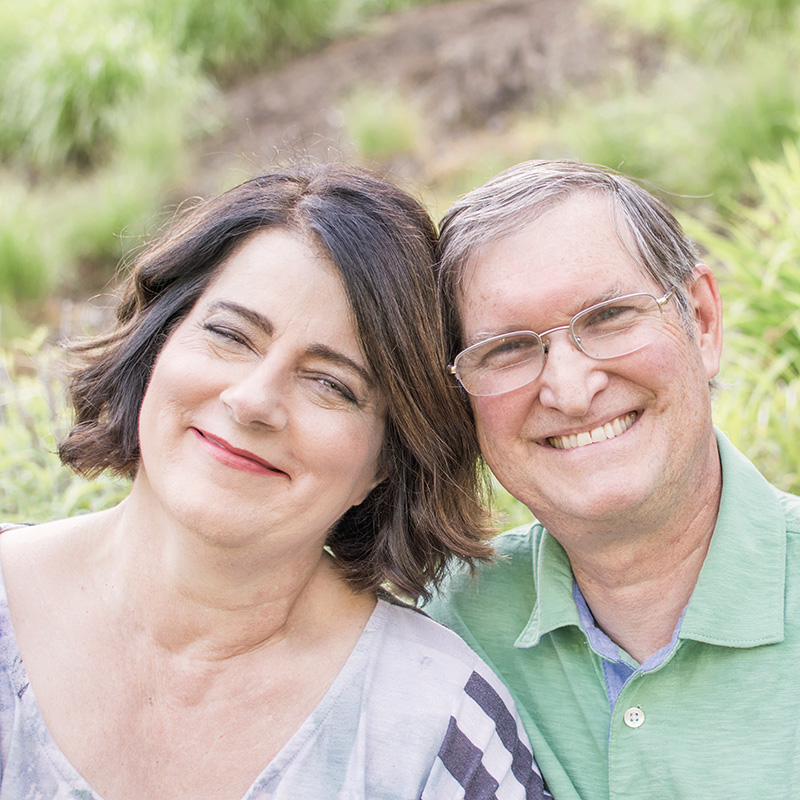 woman and man with their heads together. They are smiling and looking at the camera.